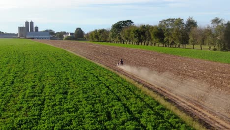 Aerial-tracking-shot-of-4-wheeler,-ATV-speeding-through-farm-field,-dust-cloud-behind