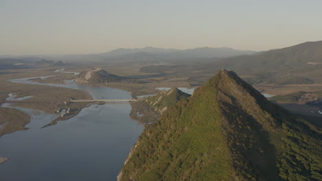 Landscape-view-of-a-river-estuary-with-two-pyramid-shaped-mountains-and-a-mountain-ridge-in-the-background-on-the-sunset