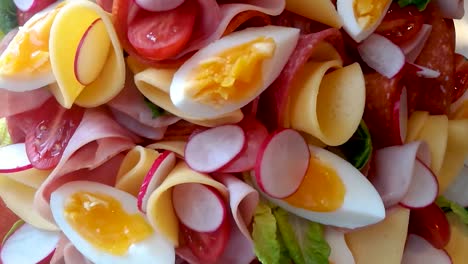 Colorful-family-food-platter-made-of-vegetables,-soft-boiled-eggs,-salami,-and-cheese,-SLIDE-ABOVE