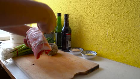 Male-hands-tying-up-pork-belly-to-a-roll-with-butcher's-twine-in-home-kitchen-setting