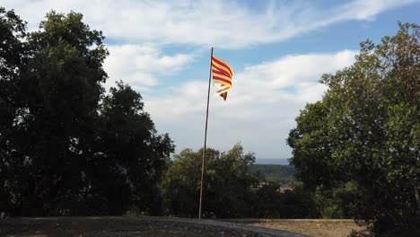 Zoom-in-on-Catalan-flag-on-top-of-a-hill,-overlooking-hills-with-a-cloudy-sky