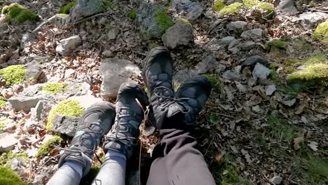 Feet-of-hiker-couple-resting-on-rocky-ground-in-deep-forest-on-early-autumn-sunny-day,-Part-1,-PAN-RIGHT