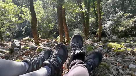 Feet-of-hiker-couple-resting-on-rocky-ground-in-deep-forest-on-early-autumn-sunny-day,-Part-2,-PAN-RIGHT