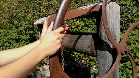 Womans-hand-rotating-wheel-on-old-rusty-water-well,-STILL