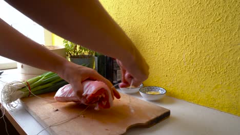 Male-hands-tying-up-rolled-pork-belly-with-butcher's-twine-in-home-kitchen-setting