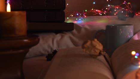 Gemütlicher-Hintergrund-Eines-Offenen-Buches-Auf-Einem-Bett,-Neben-Einem-Becher-Und-Umgeben-Von-Bunten-Weihnachtslichtern