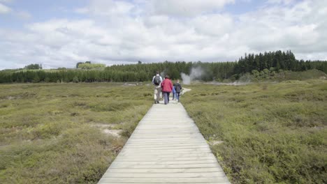 A-shot-following-a-family-as-they-walk-along-a-wooden-path-at-Craters-of-the-Moon-in-Taupo,-NZ