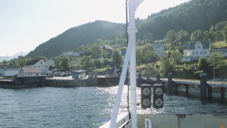 Norwegian-ferry-driving-on-fjord-from-Volda-to-Lauvstad,-arriving-at-habour,-against-the-sun,-Norway