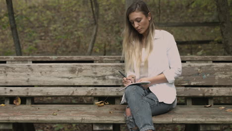 Young-female-sits-in-a-forest-park-with-a-sketch-pad-slider-dolly-shot