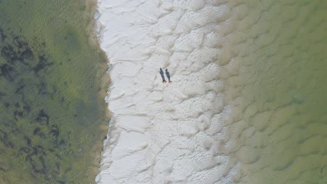 Aerial-vertical-view-of-a-couple-walking-through-out-a-sand-bank-with-water-on-both-sides