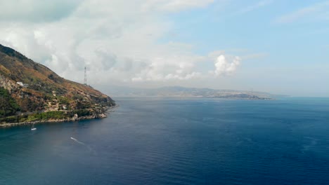 AERIAL-DOLLY-IN:-Drone-flying-above-the-Tyrrhenian-Sea,-with-an-incredible-view-of-Sicily's-coast-from-Calabria,-Italy