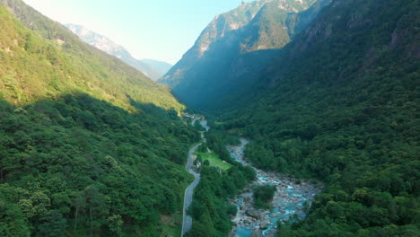 Wide-arial-view-of-a-scenic-tree-covered-valley-with-a-glacier-river-its-way-through-the-valley,-Verzasca-valley,-Switzerland