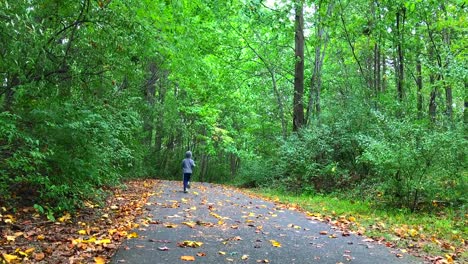 A-boy-running-through-a-green-forest-with-fallen-yellow-leaves-on-the-ground