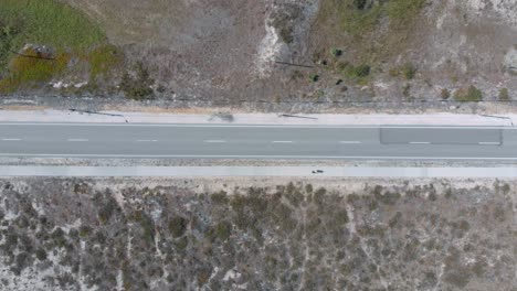 Aerial-vertical-view-of-a-road-in-a-natural-reserve-with-sand-and-bushes-on-both-sides