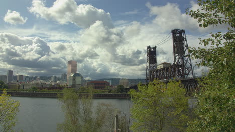 Lift-bridge,-towering-cumulus-clouds,-riverfront-cityscape,-pan-left