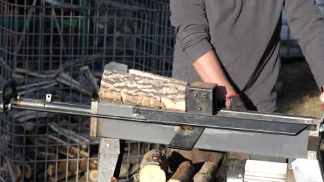Man-using-log-cutting-machine-to-chop-wood,-throwing-firewood-in-a-pile,-rack-focus