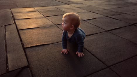 Happy-toddler-boy-sits-facing-sunset-turns-to-and-lays-down-on-rubber-playground-mat-on-warm-summer-evening