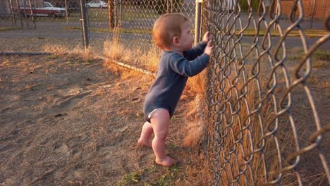 Happy-toddler-boy-stands-against-fence-near-home-plate-and-shakes-fence