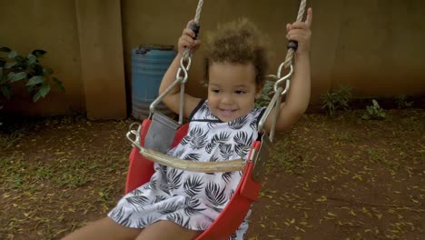 slow-motion-shot-of-a-happy-little-girl-smiling-while-on-a-rope-swing-attached-to-a-tree-in-a-backyard