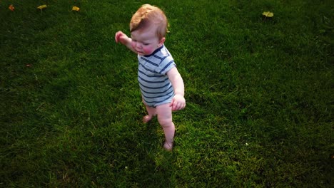 Toddler-stands-up-rises-from-ground-and-takes-first-steps-alone-in-grass-as-sun-comes-out
