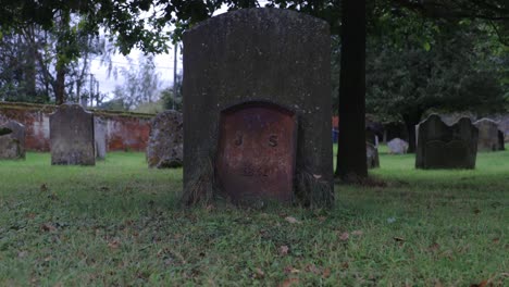 Jib-up-to-gravestone-showing,-J-S-,in-old-graveyard-with-mossy-headstones