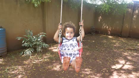 A-happy-little-mixed-raced-girl-swinging-in-a-tree-swing-in-a-backyard-showing-her-dirty-feet