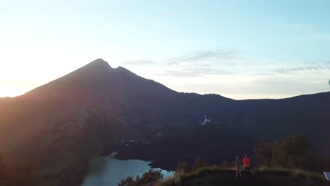 AERIAL-4K-Forward-Moving-Shot,-Standing-on-Crater-Rim-at-Sunrise-with-Mount-Rinjani-Crater-Lake-in-Background,-Indonesia