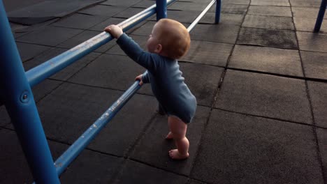Happy-toddler-boy-stands-up-on-his-own-using-blue-jungle-gym-bars