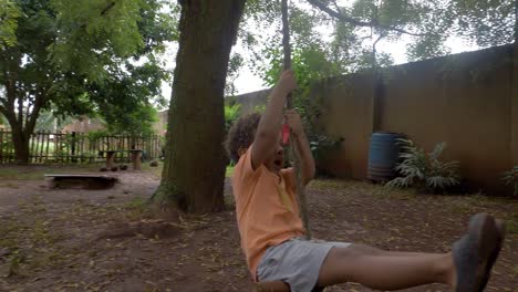 slow-motion-shot-of-a-young-boy-holding-onto-a-rope-swing-attached-to-a-tree-in-a-backyard