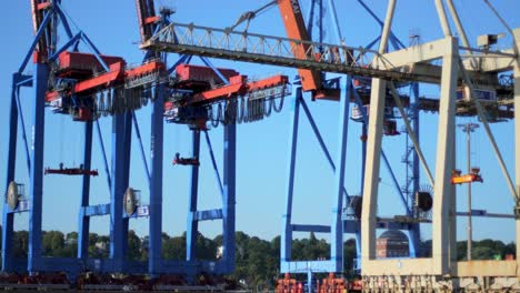 Eine-Reihe-Riesiger-Containerkräne-In-Einem-Industriehafen-Mit-Einem-Kleineren-Kran-Im-Vordergrund-Und-Einem-Klaren-Blauen-Himmel-Im-Hintergrund