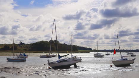 Handheld-shot-of-boats-in-the-mud-at-low-tide-in-a-river-with-a-stunning-cloudy-sky-and-a-bird-wading-into-frame
