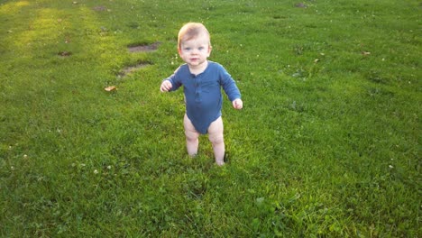 Happy-toddler-boy-stands-up-alone-in-grass-field,-almost-loses-balance,-and-smiles