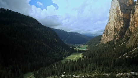 Sideways-flight-left-to-right-across-a-beautiful-alpine-mountain-valley-with-sheer-rock-on-the-right-and-wooded-hills-on-the-left