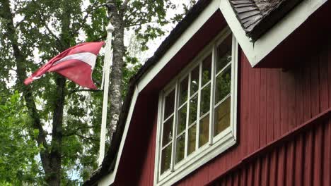 Lettische-Flagge-Weht-Neben-Einem-Alten-Roten-Haus