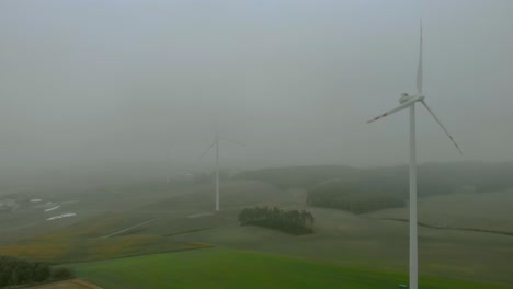 Aerial-footage-close-up-to-wind-farm,-windmill-during-fog,-grey-landscape-around,-renewable-energy-in-the-open-field,-below-natural-landscape,-green-energy-is-important