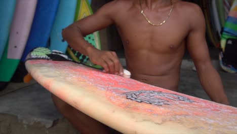Young-Man-Waxing-Surfboard-In-Surf-Shop,-Lombok-Indonesia
