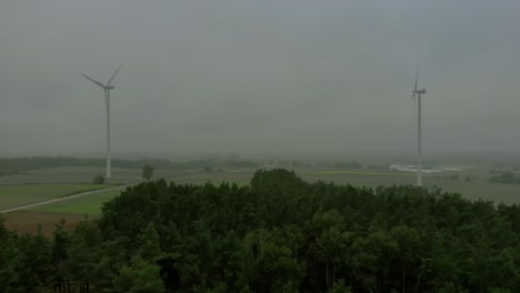 Aerial-footage-near-windmills-near-hight-trees,-foggy-weather-conditions-on-the-horizon,-drone-shoot-video-4k