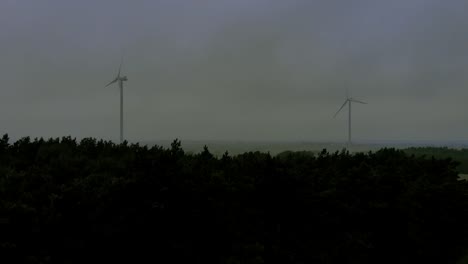 Luftaufnahmen-In-Der-Nähe-Von-Windmühlen-In-Der-Nähe-Von-Hohen-Bäumen,-Neblige-Wetterbedingungen-Am-Horizont,-Drohnenaufnahmevideo-4k