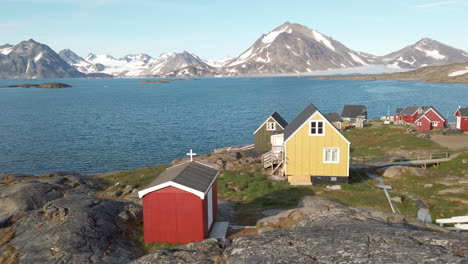 Peaceful-and-colorful-seaside-village-in-Greenland-with-snow-capped-mountains-in-distance-and-small-homes-in-foreground-with-tiny-red-church