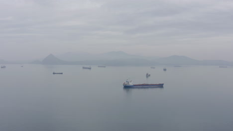 Ships-at-anchorage-waiting-area-in-a-calm-weather,-with-mountain-ridge-in-far-distance-on-the-overcast-day