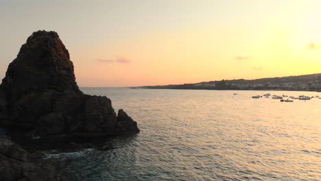Aerial-circle-around-small-rock-island-revealing-beautiful-coastal-town-and-sunset