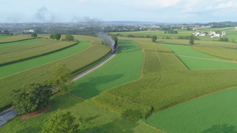 An-Aerial-View-of-a-Steam-Train-Puffing-Smoke-Through-Farm-Countryside-on-a-Sunny-Summer-Day-with-Green-Fields