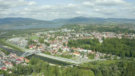 Drone-shot-of-charmingly-located-Zywiec-city---between-river-and-lake-among-mountains,-full-of-green-trees