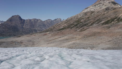 Luftbild-Aus-Niedriger-Höhe-Von-Einer-Drohne,-Die-über-Das-Eisfeld-Des-Gletschers-In-Grönland-Fliegt,-Mit-Zerklüftetem-Gelände-Aus-Steilen-Berghängen-Und-Zerklüfteten-Gipfeln,-Die-Bis-Zum-Klaren-Blauen-Himmel-Reichen