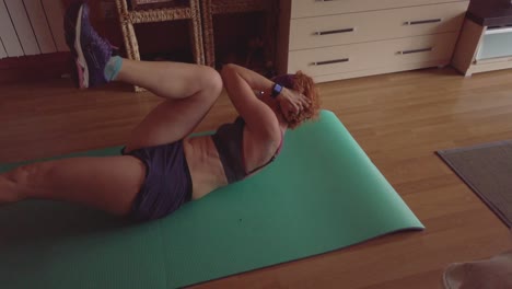 A-45-years-old-red-head-woman-doing-exercise-at-home,-She´s-touching-her-knees-with-her-elbows