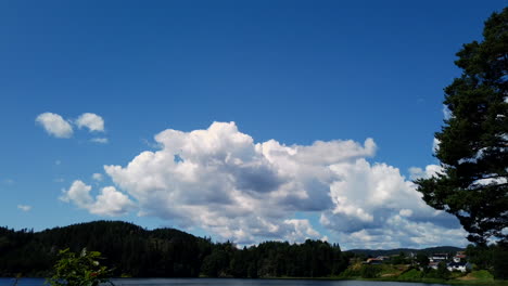 Time-lapse-shot-of-clouds-building,-on-the-blue-sky,-above-Norwegian-nature-and-the-Birkeland-town,-on-a-sunny-day,-in-south-Norway