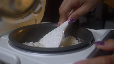 Static-close-up-of-hand-stirring-rice-in-rice-cooker,-steam-rising
