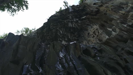 Water-dripping-down-interesting-curvy-cliff-rock-face,-slow-mo-up-shot