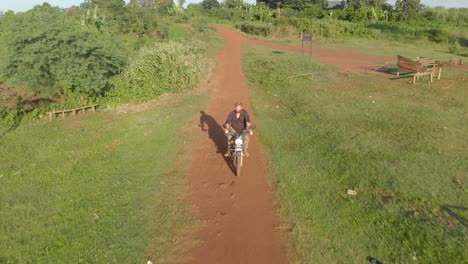 Aerial-shot-tracking-from-the-front-a-ginger-haired-bearded-explorer-riding-on-a-African-rural-dirt-road-on-a-motor-cycle