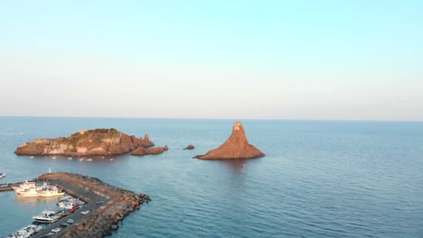 Aerial-tracking-forward,-marina-and-tall-rocky-island-off-coast-of-Sicily